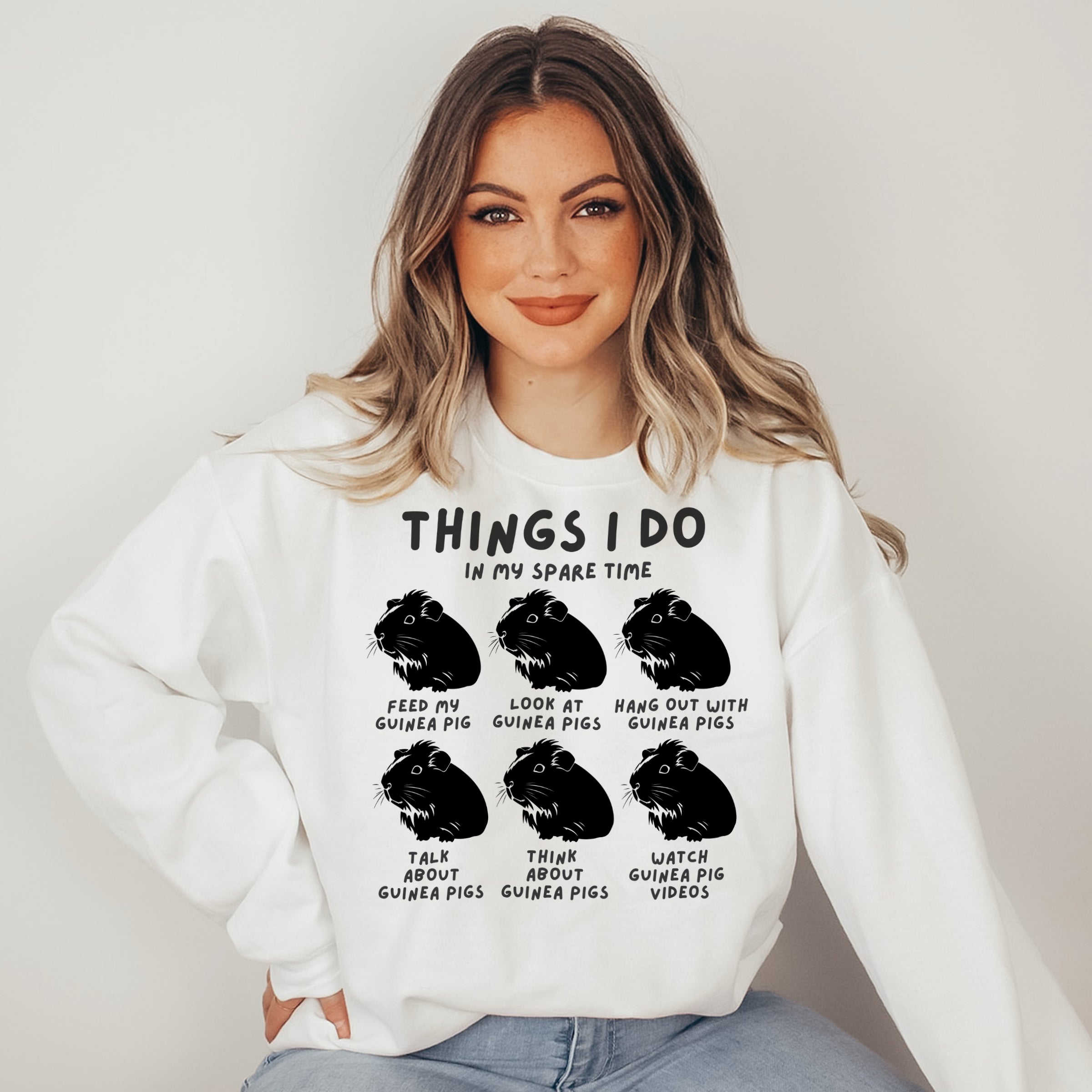 Woman wearing a white sweatshirt with black text and guinea pig illustrations on a plain background
