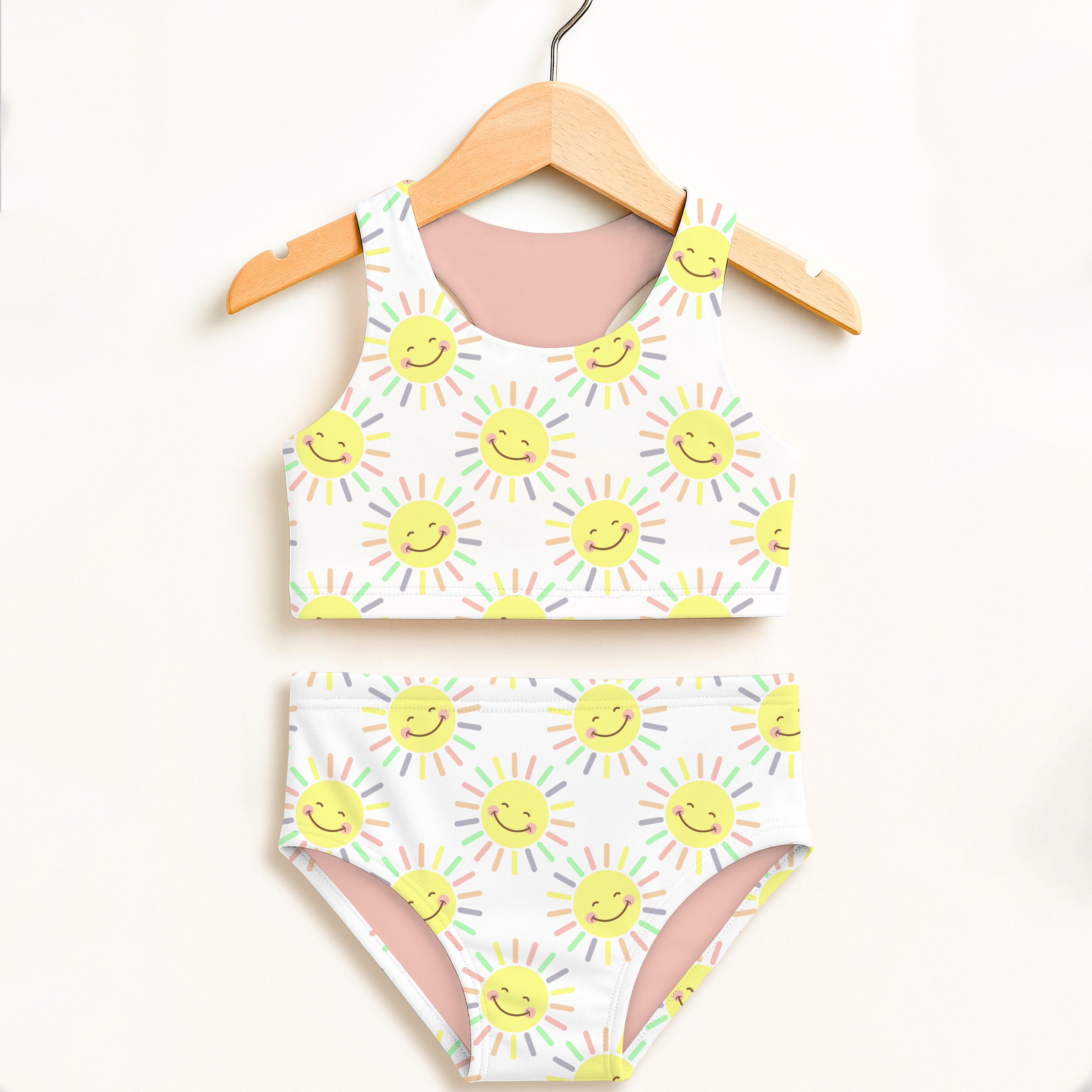 White two-piece girls swimsuit with yellow smiling suns pattern pastel rainbow rays pink lining halter neckline upf 50+