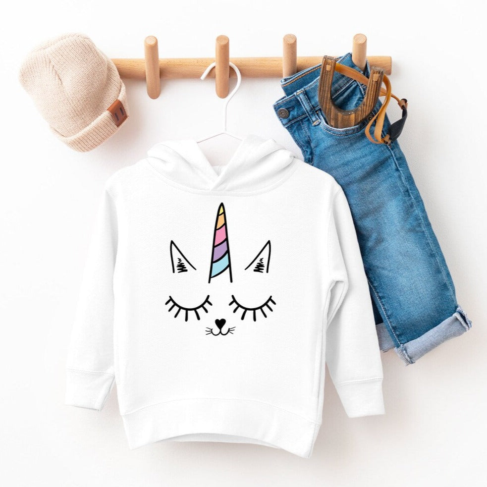 Kids white unicorn graphic hoodie and blue jeans outfit, hanging with beige knit hat.