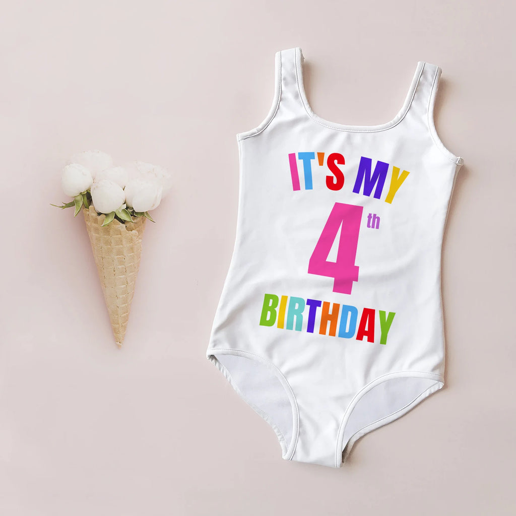 A white swimsuit for girls with 'IT'S MY 4th BIRTHDAY' printed in colorful letters on the front, displayed next to a ice cream cone with white flowers on top.