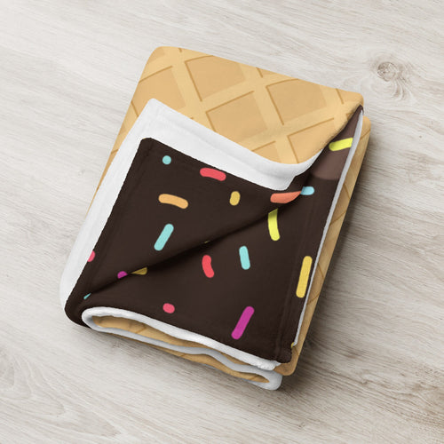 A cozy chocolate ice cream cone blanket folded to resemble a waffle cone with colorful sprinkles design