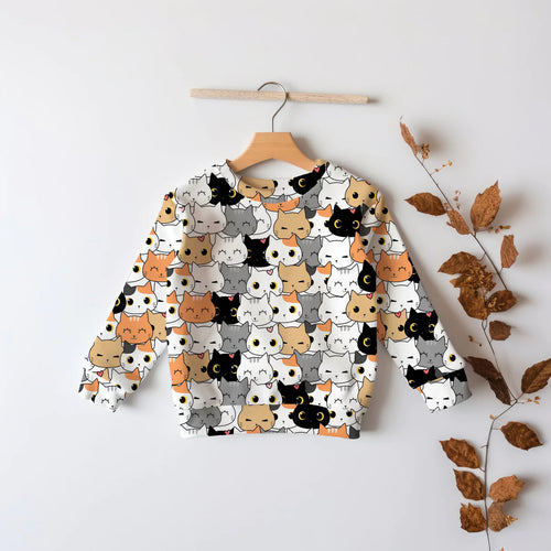 A sweatshirt with various cartoon cat designs printed on it, displayed on a wooden hanger against a white background, with some dried leaves at the bottom right.