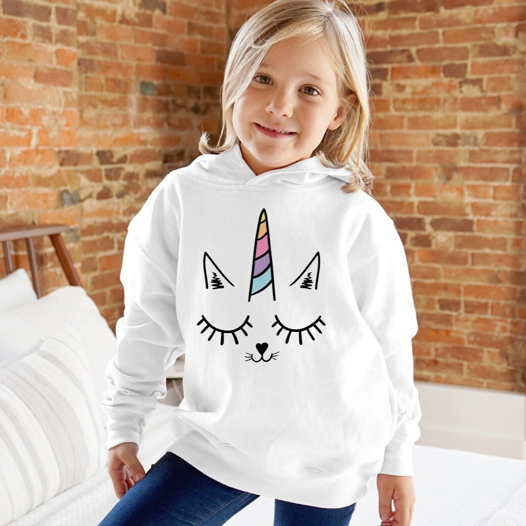 Smiling child in white hoodie with unicorn cat face graphic, cozy home setting, kids clothing