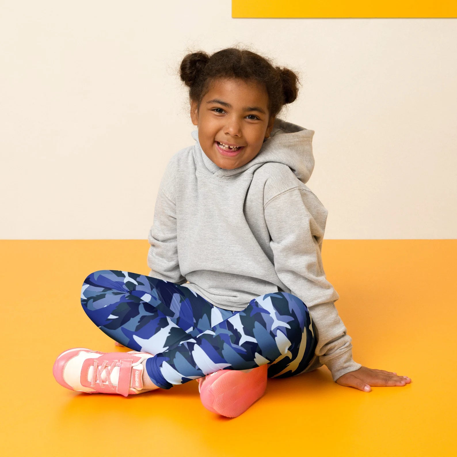 A young girl wearing kids blue shark buttery soft blue camouflage leggings with a gray hoodie and pink sneakers