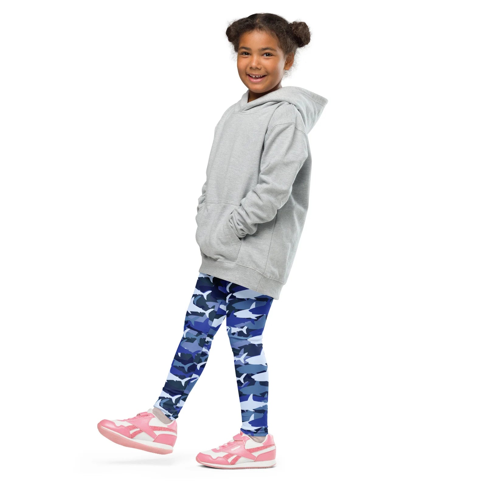 A child wearing kids blue shark buttery soft leggings with blue shark pattern and a light gray hooded sweatshirt
