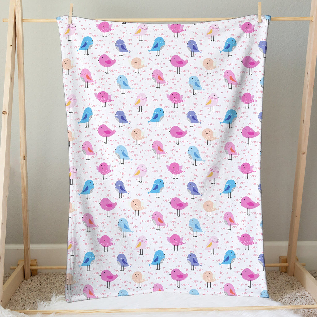 A soft white girls colorful birds blanket with playful pink blue and purple cartoon bird patterns