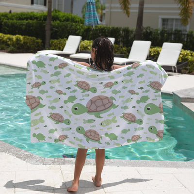 White beach towel featuring a playful pattern of green and brown turtles swimming among small fish for kids