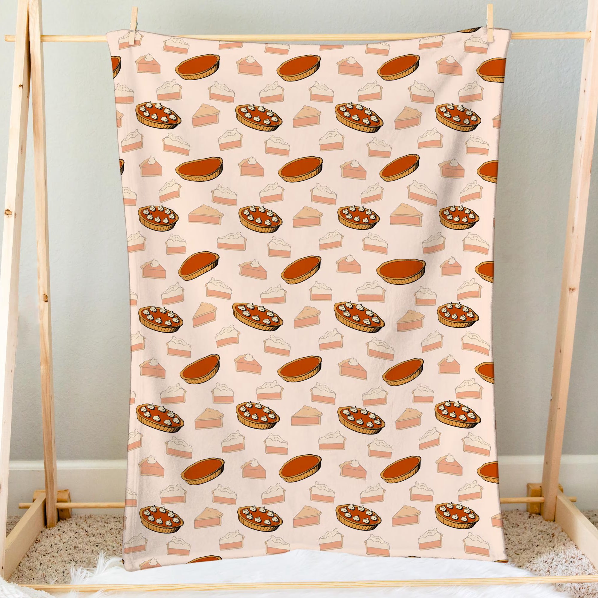 A soft cream-colored pumpkin pie thanksgiving blanket with playful orange and beige pie illustrations