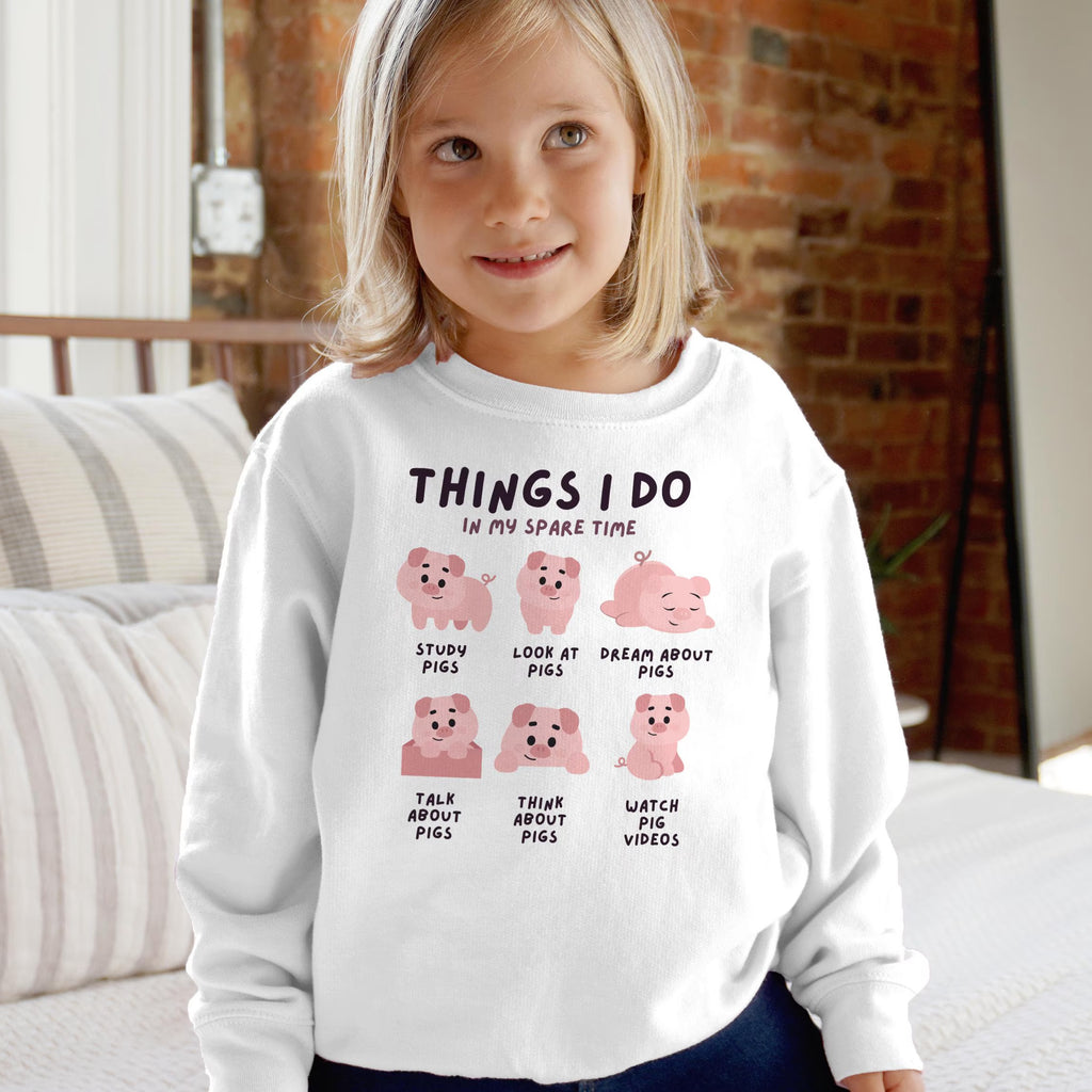 White long-sleeved kids sweatshirt with pink pig illustrations and text things i do in my spare time cozy and fun