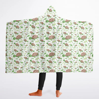 A cozy white hooded wearable blanket for kids featuring a playful green and brown sea turtle pattern