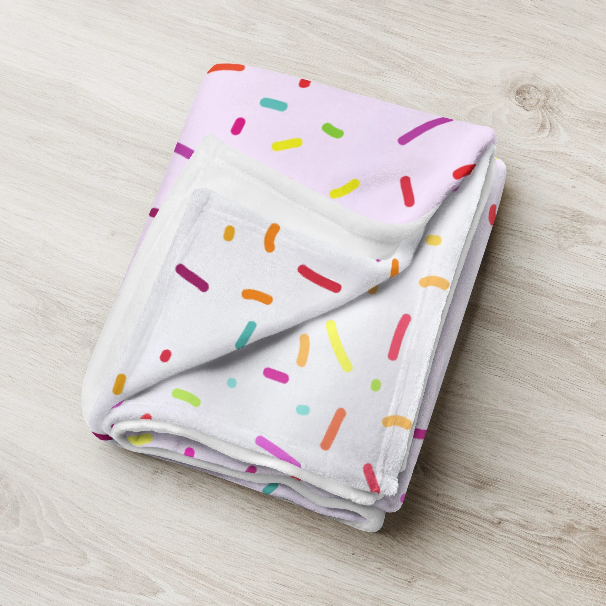 A soft girls colorful sprinkles ice cream blanket folded with rainbow pattern on light pink and white background