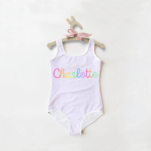 A white one-piece girls swimsuit with custom rainbow charlotte name hanging on a wooden bunny-shaped hanger