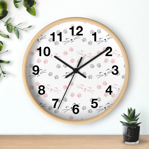 A round silent wood wall clock with light wood frame white face pink and gray cat paw prints and whisker faces