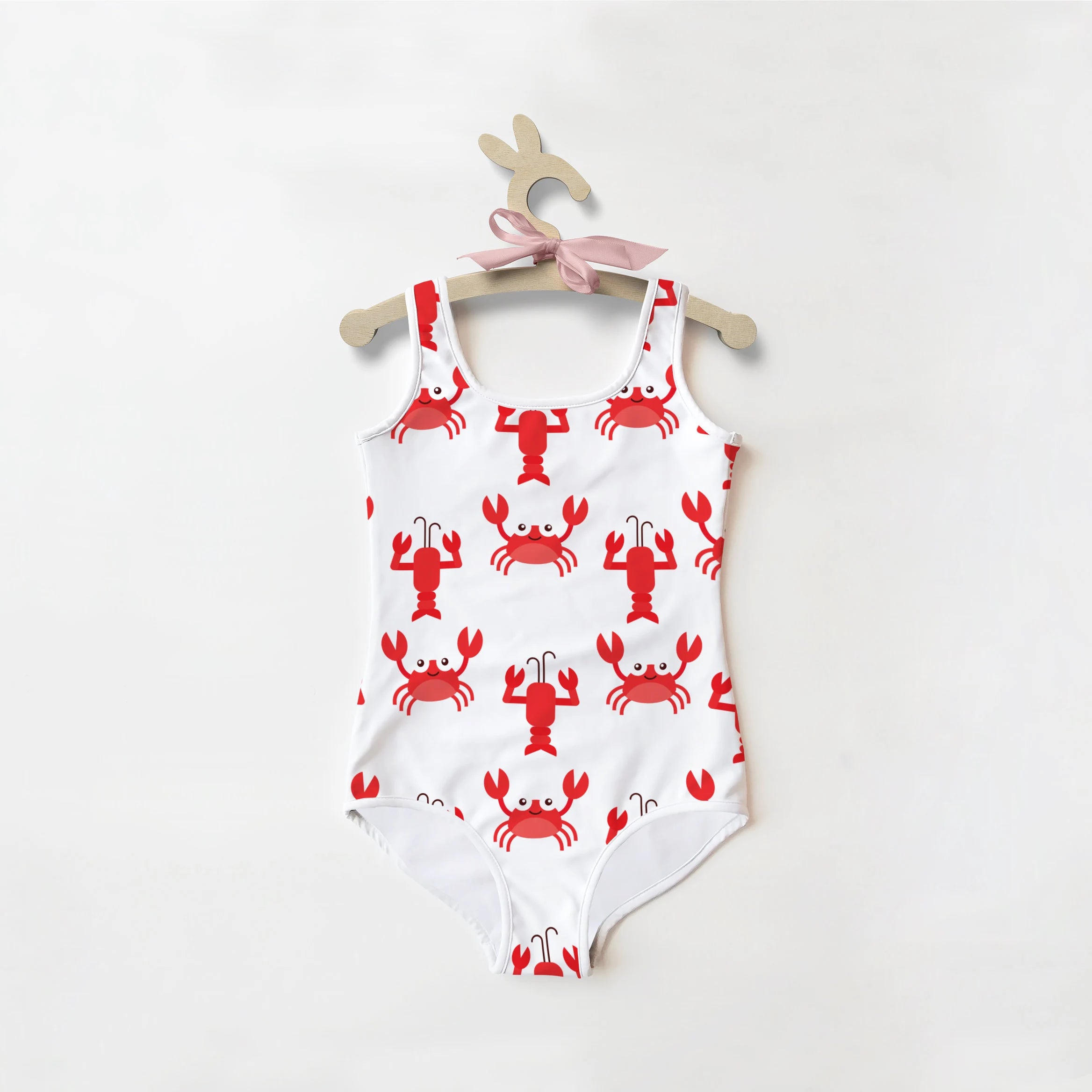 White girls one-piece swimsuit with red crab and lobster prints hanging on wooden hanger with pink ribbon