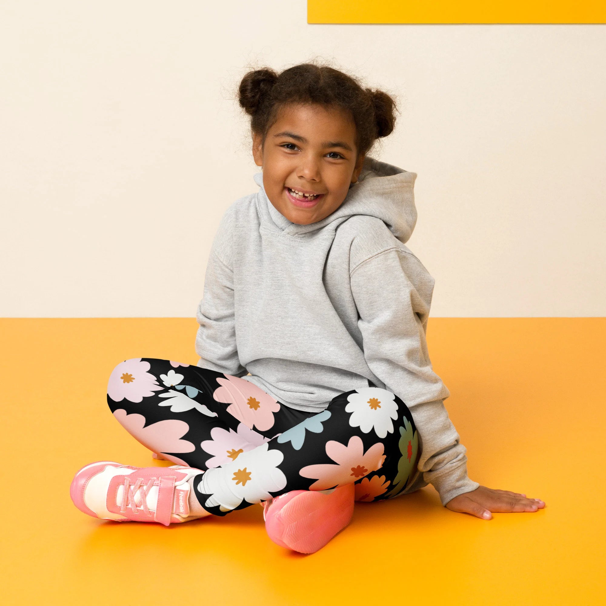 A child wearing girls flower buttery soft gray leggings with pink white and green floral patterns and a gray hoodie