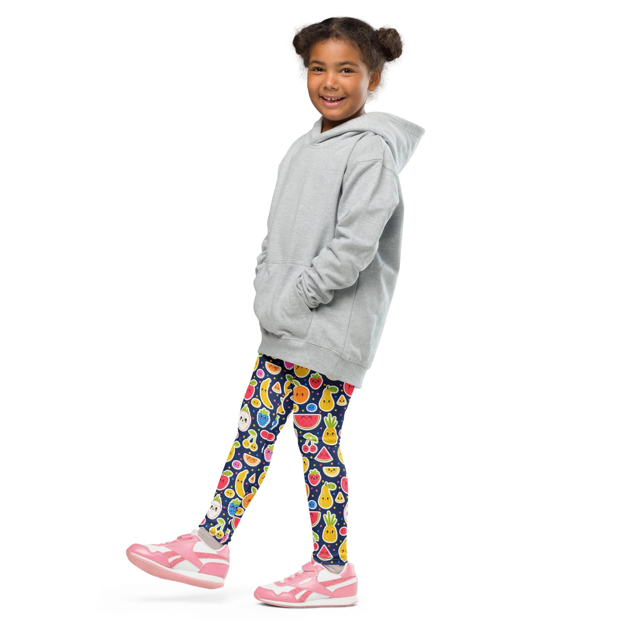 A child wearing girls emoji fruit buttery soft leggings with colorful fruit patterns and a light gray hooded sweatshirt