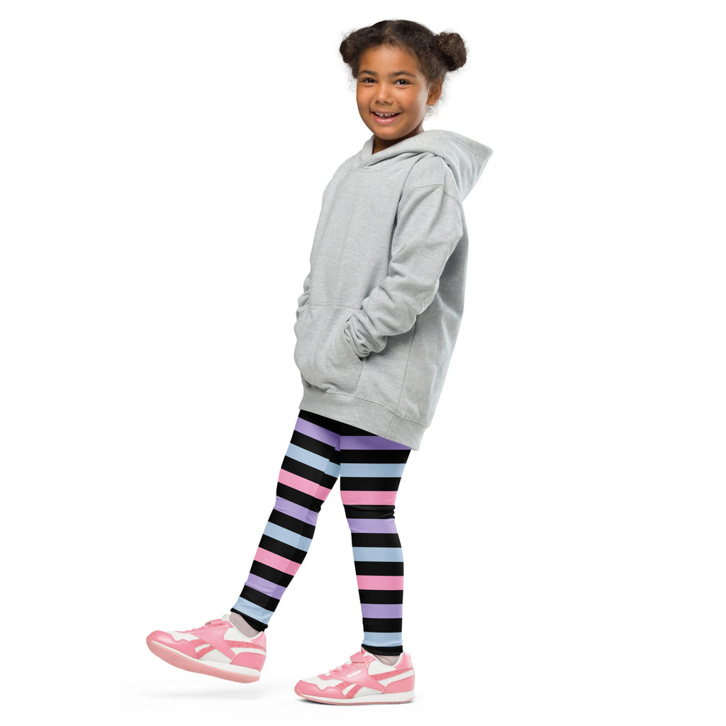 A young girl wearing girls colorful striped buttery soft leggings in purple black and blue with a light gray hooded sweatshirt