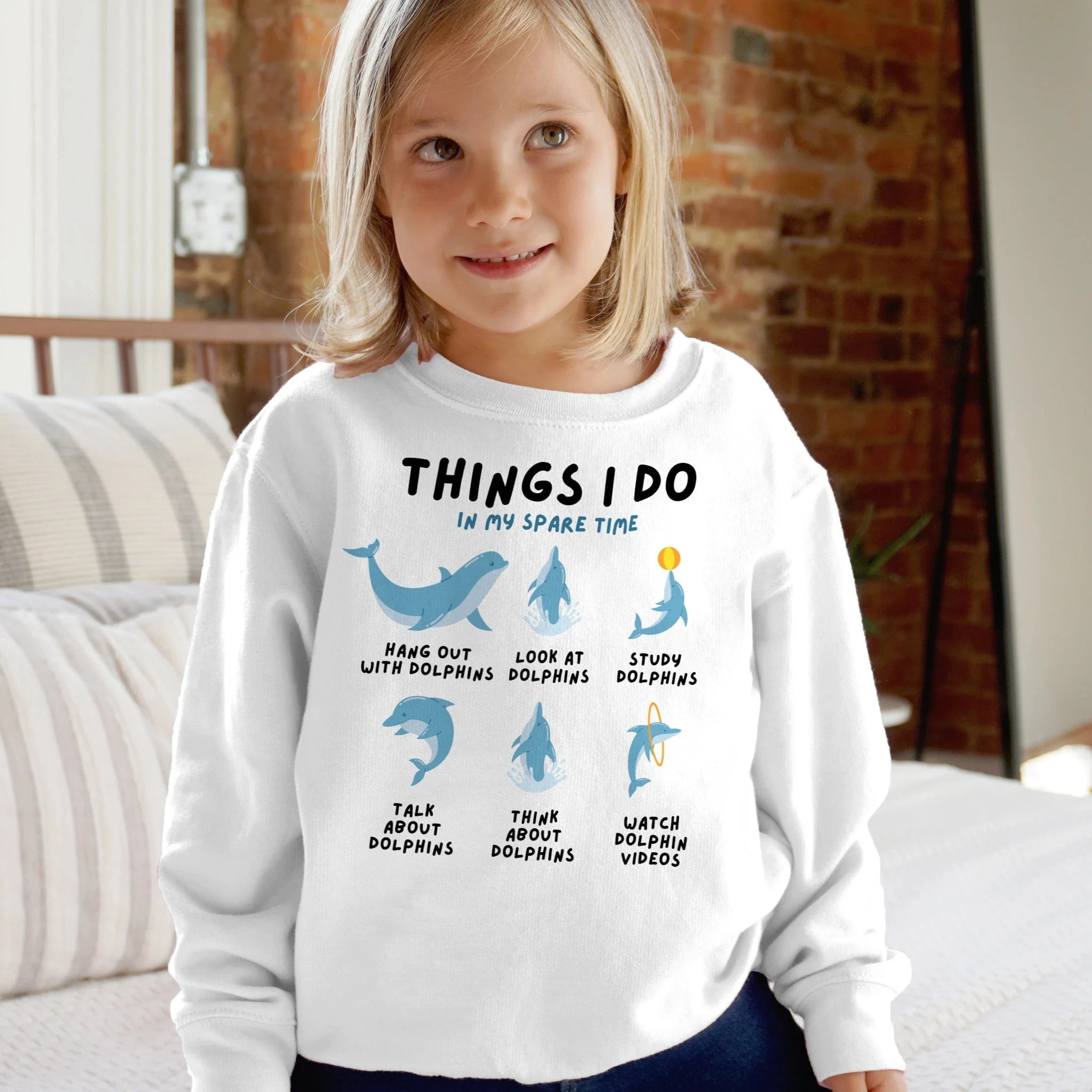 White kids long-sleeved sweatshirt with blue dolphin illustrations and black text reading things i do in my spare time