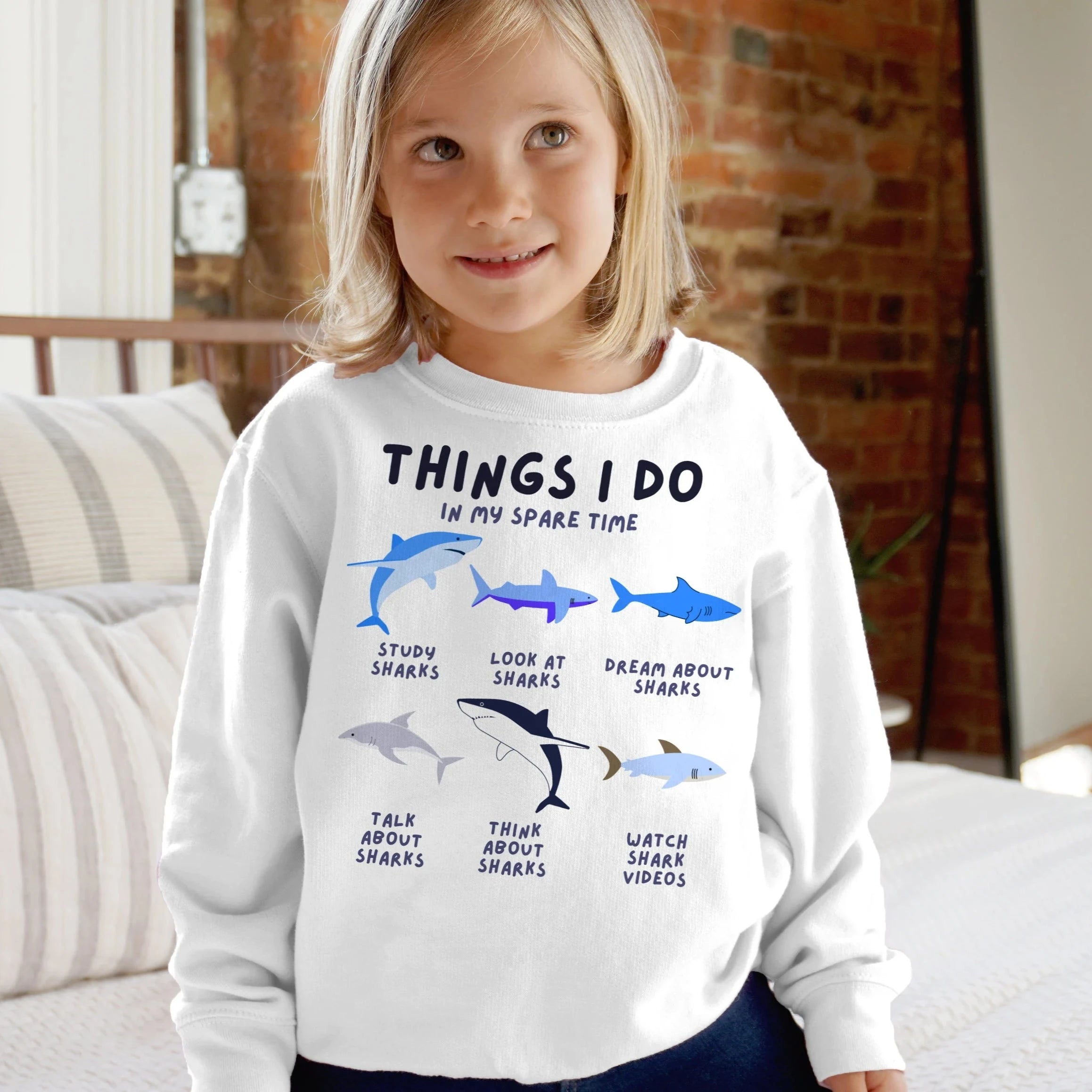 Kids white long-sleeved sweatshirt with blue and gray shark illustrations and black text things i do in my spare time