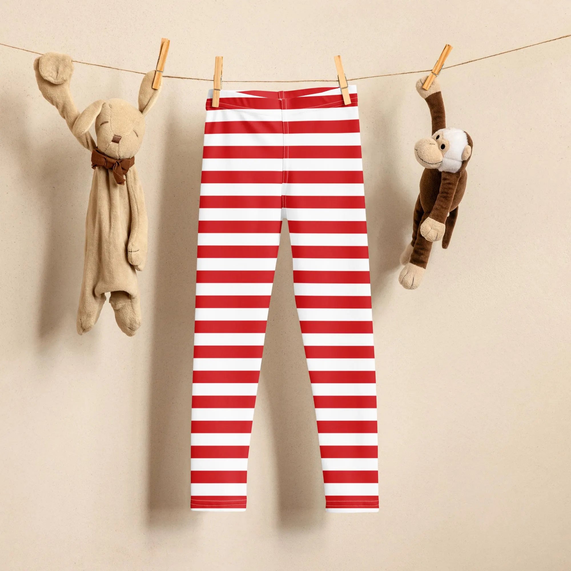 Red and white horizontally striped buttery soft christmas leggings for kids hanging on a clothesline