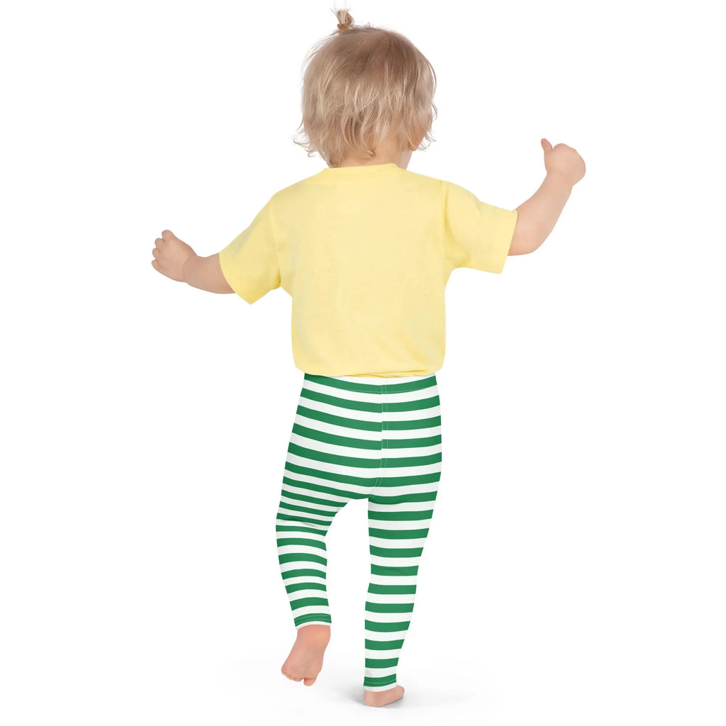 A toddler wearing soft green striped buttery Christmas leggings and a yellow short-sleeved shirt