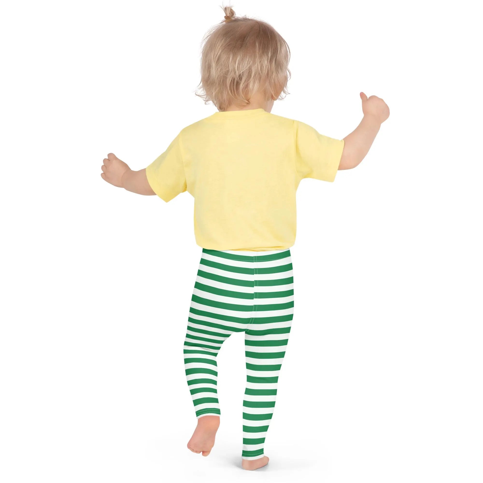 A toddler wearing soft green striped buttery Christmas leggings and a yellow short-sleeved shirt