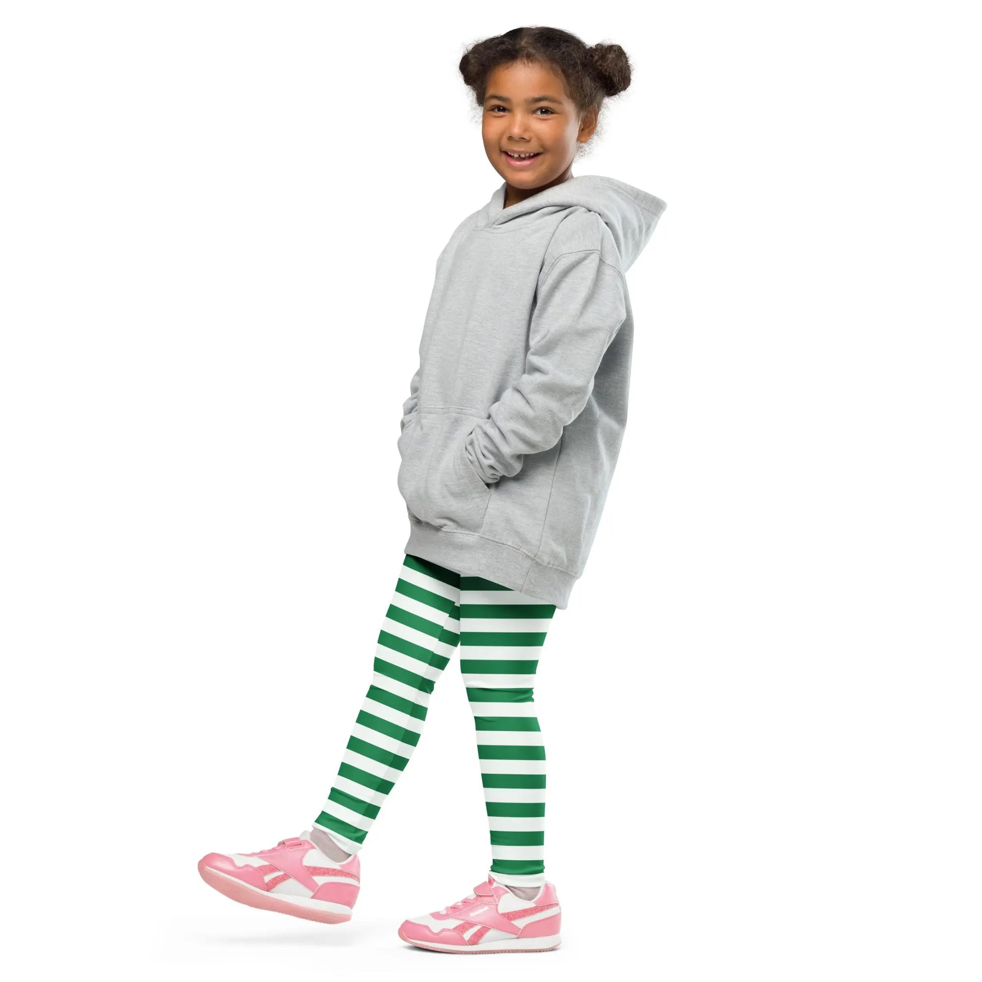 A young girl wearing green striped buttery soft Christmas leggings for kids paired with a light gray hooded sweatshirt