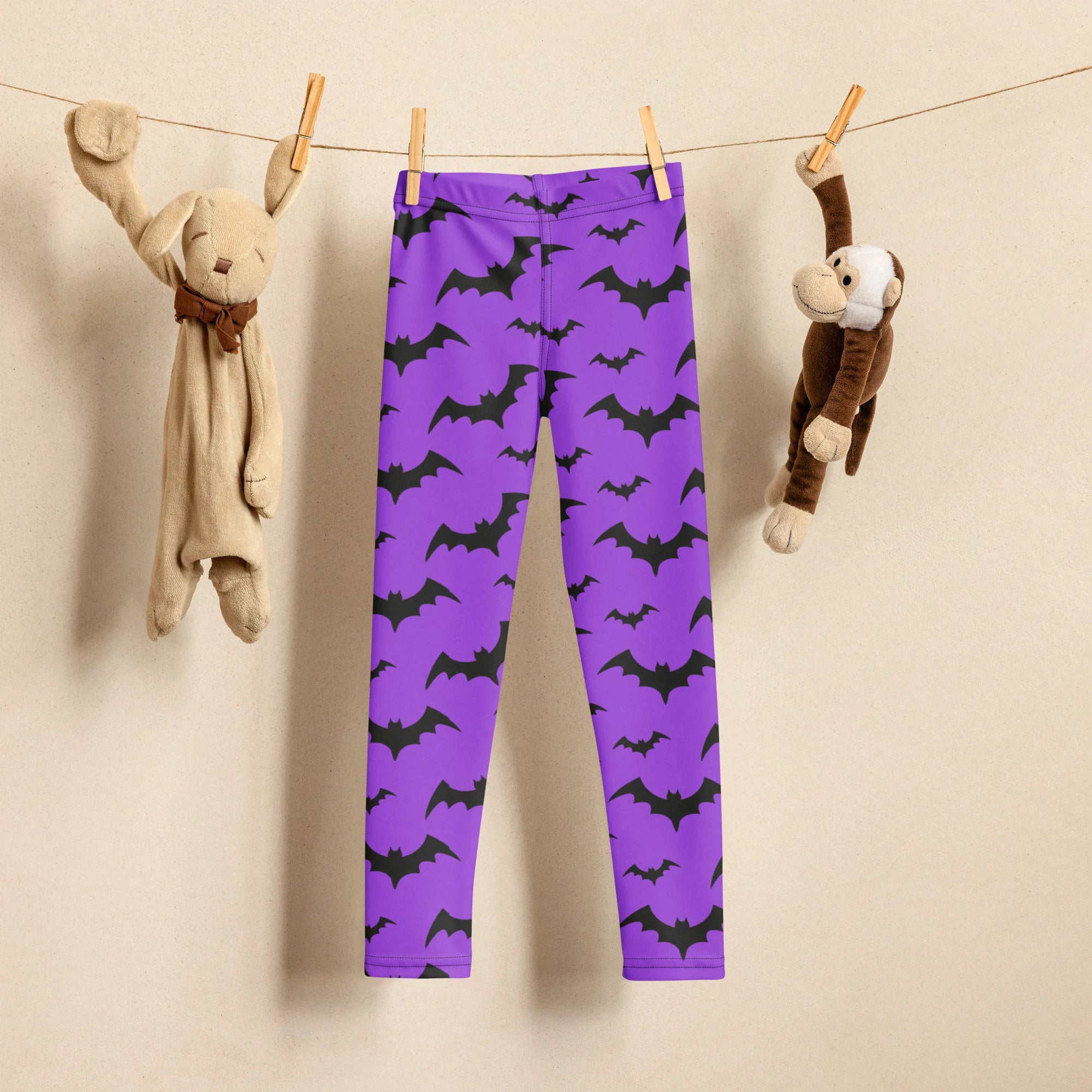Kids purple bats halloween buttery soft leggings with repeating black bat pattern hanging on a clothesline