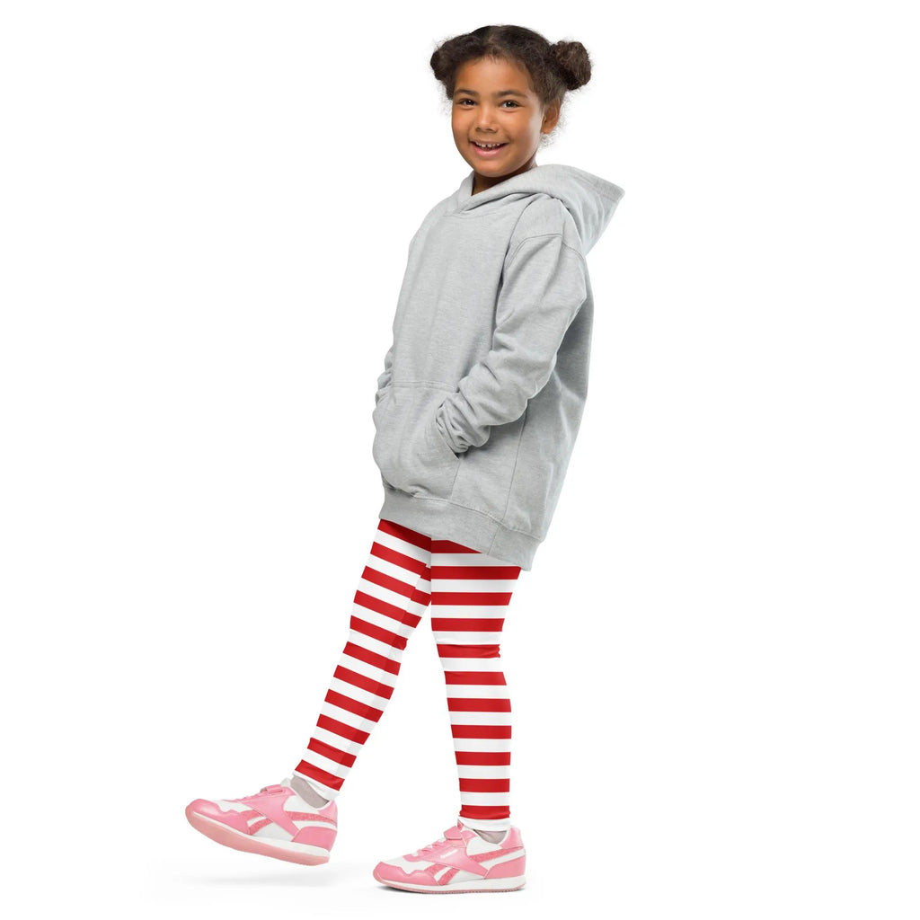 A young girl wearing red striped buttery soft Christmas leggings for kids with gray hoodie and pink sneakers