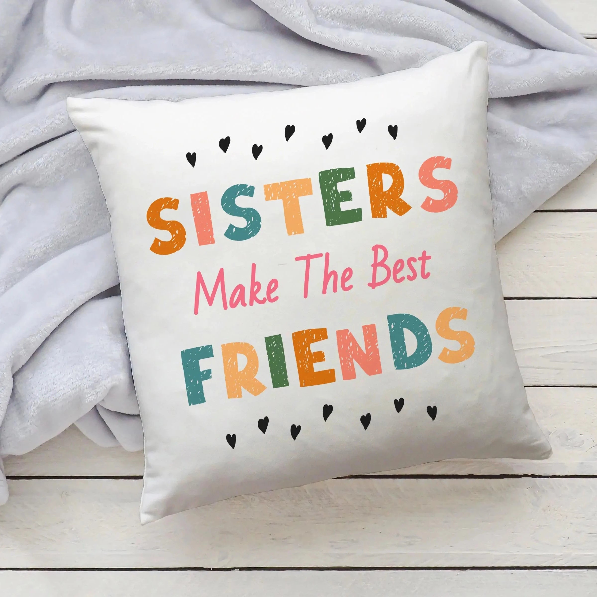 White throw pillow with colorful distressed lettering and black hearts reading sisters make the best friends
