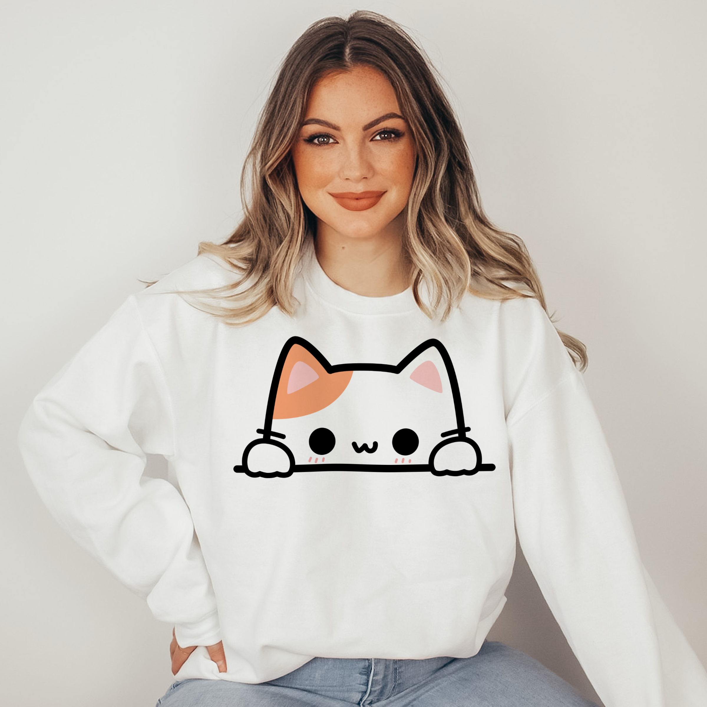 Woman wearing a white sweatshirt with a cat face design on a plain background