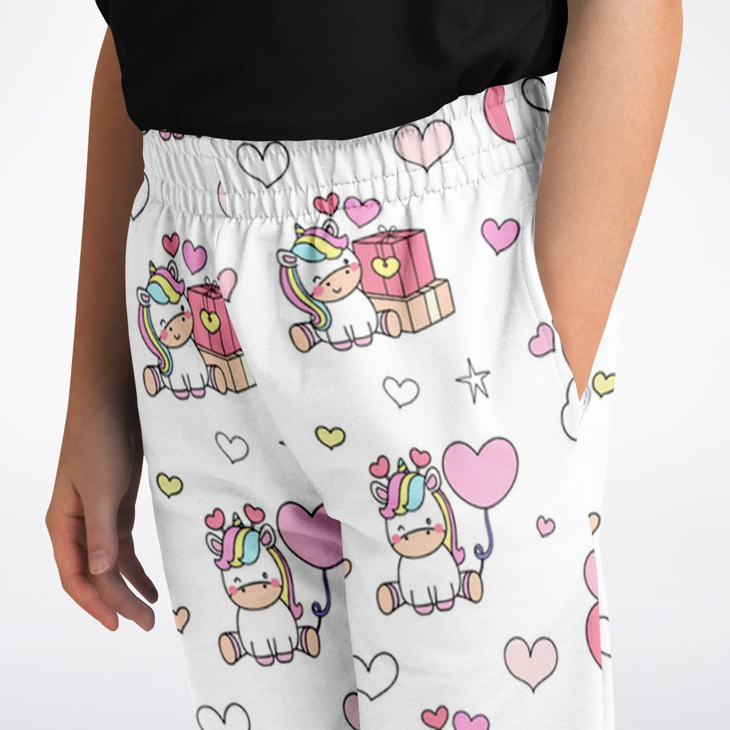 Girls unicorn birthday jogger pants in white with playful cartoon unicorns rainbow manes pink hearts and gift boxes pattern