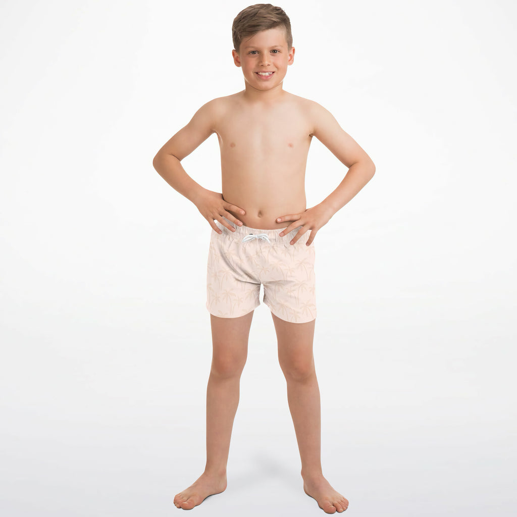 A boy wearing boys light peach palm tree quick drying swim trunks in light pink with white drawstring and subtle pattern