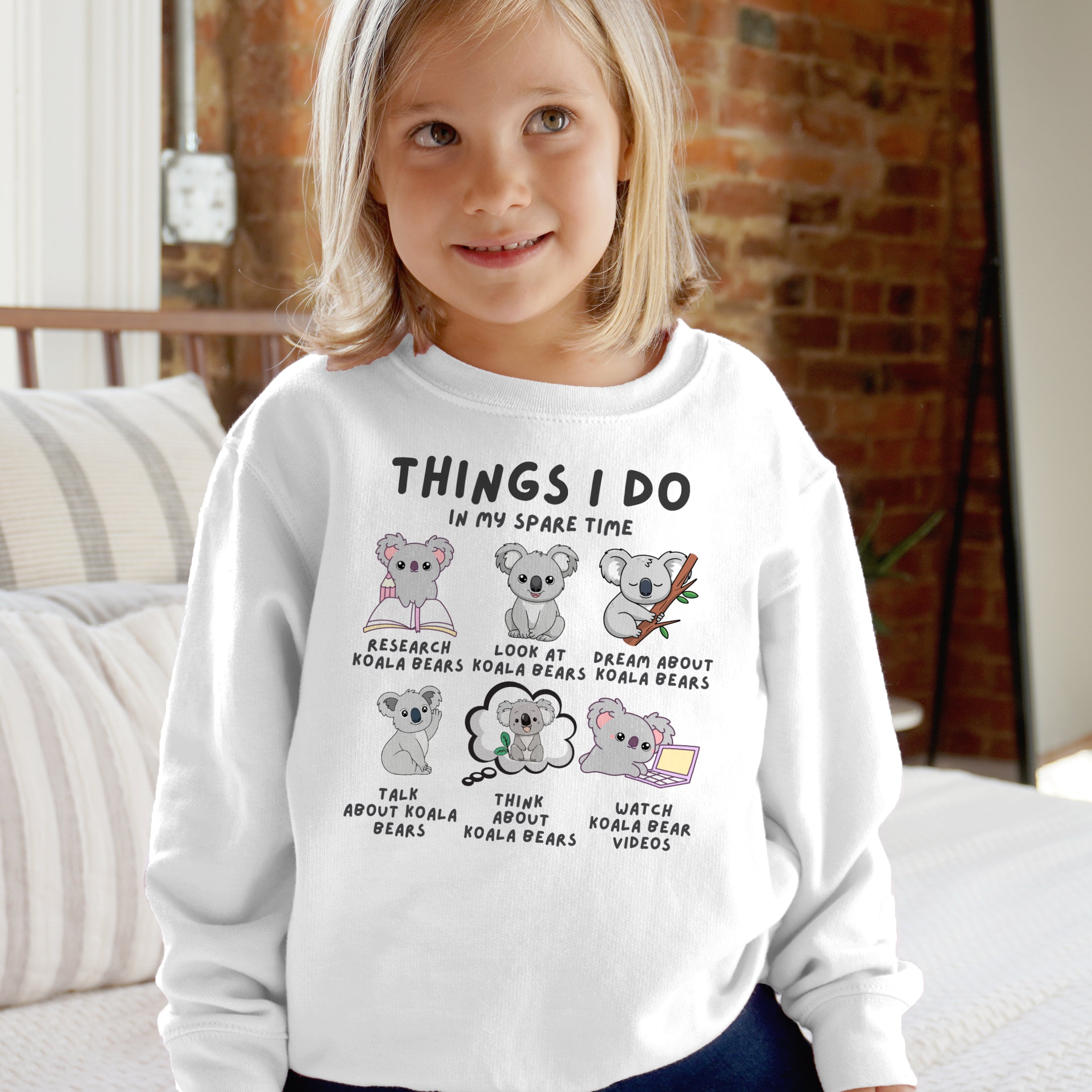 Child wearing a white sweatshirt with cartoon koalas and text in a casual indoor setting.