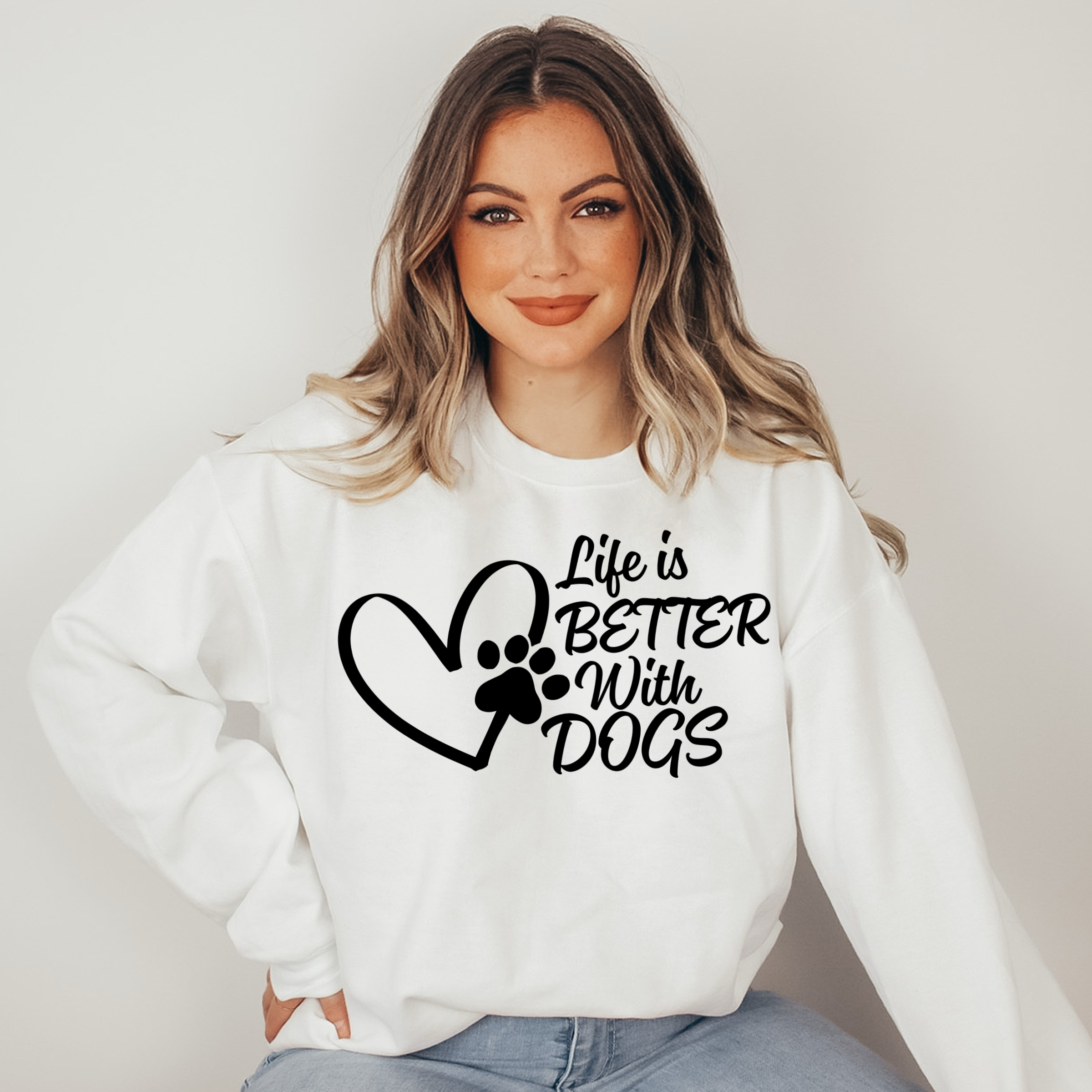 Woman wearing a white sweatshirt with 'Life is Better with Dogs' text and paw print design.
