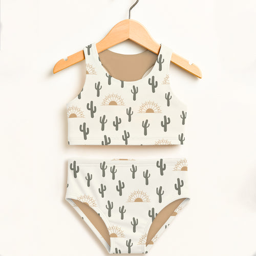 White girls desert cactus sunrise two-piece swimsuit with gray cactus and tan sunburst patterns on wooden hanger
