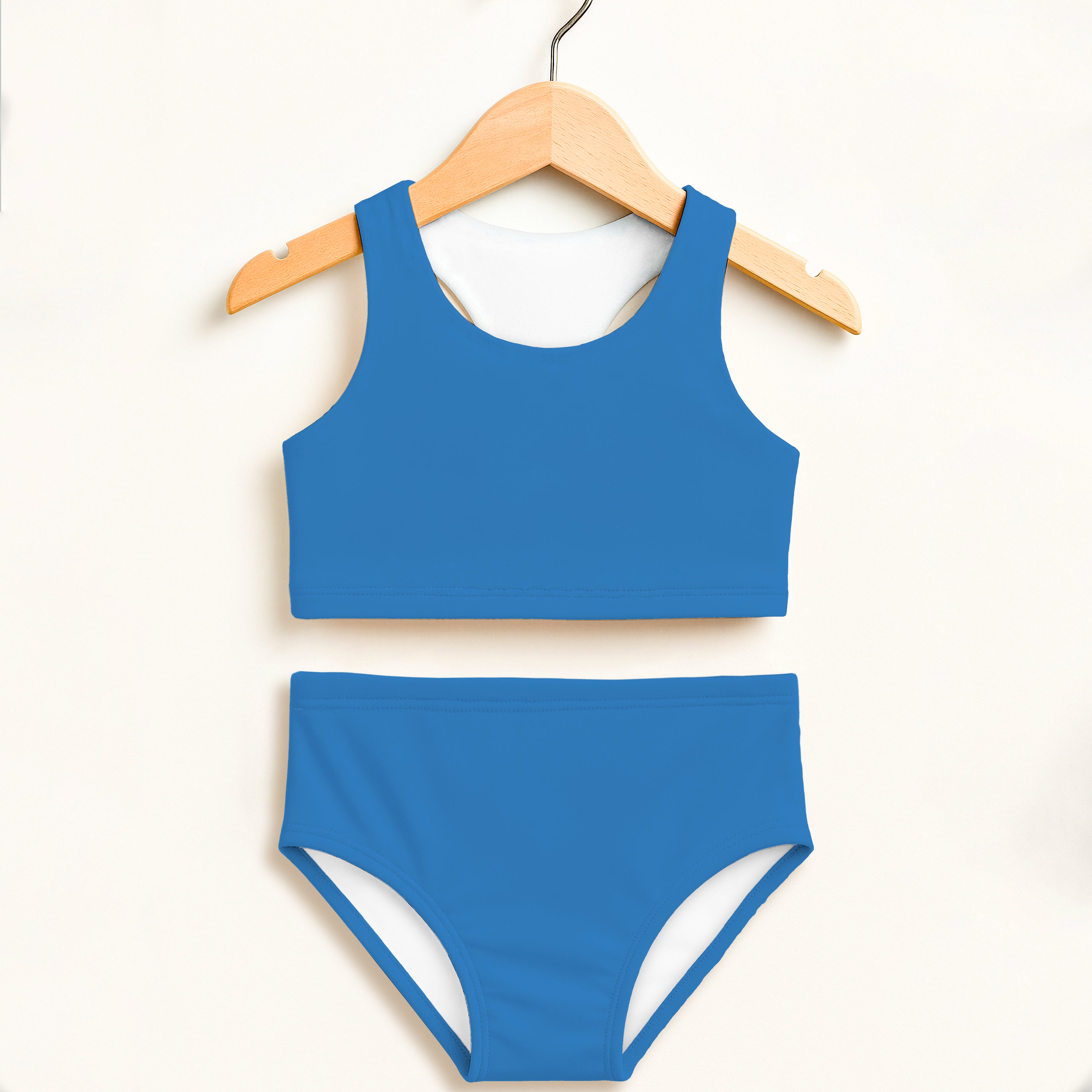 Girls blue two piece swimsuit with white lining hanging on wooden hanger featuring double layered upf 50+ fabric