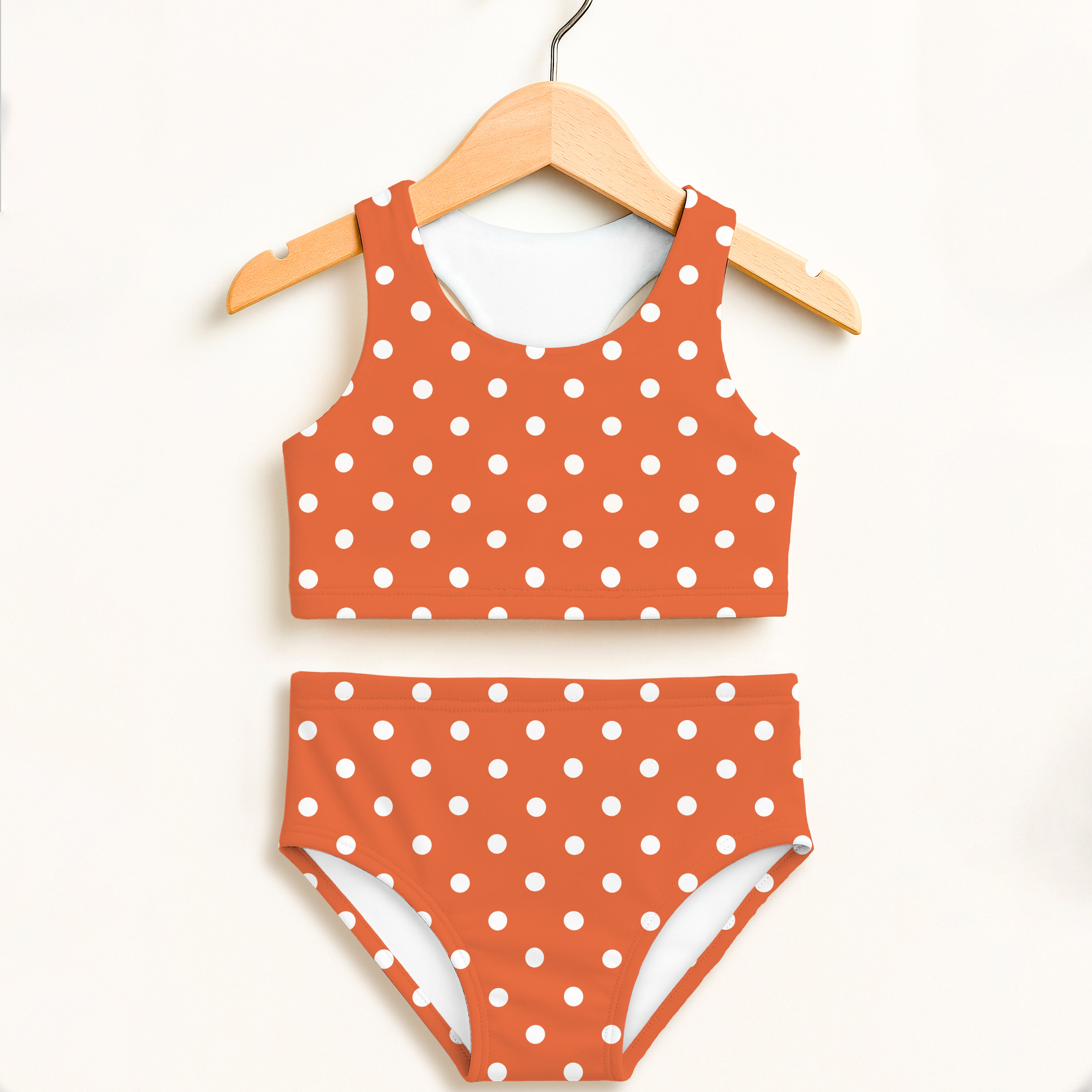 Girls orange and white polka dot two piece swimsuit with double layered upf 50 plus high waisted comfort hanging on wooden hanger