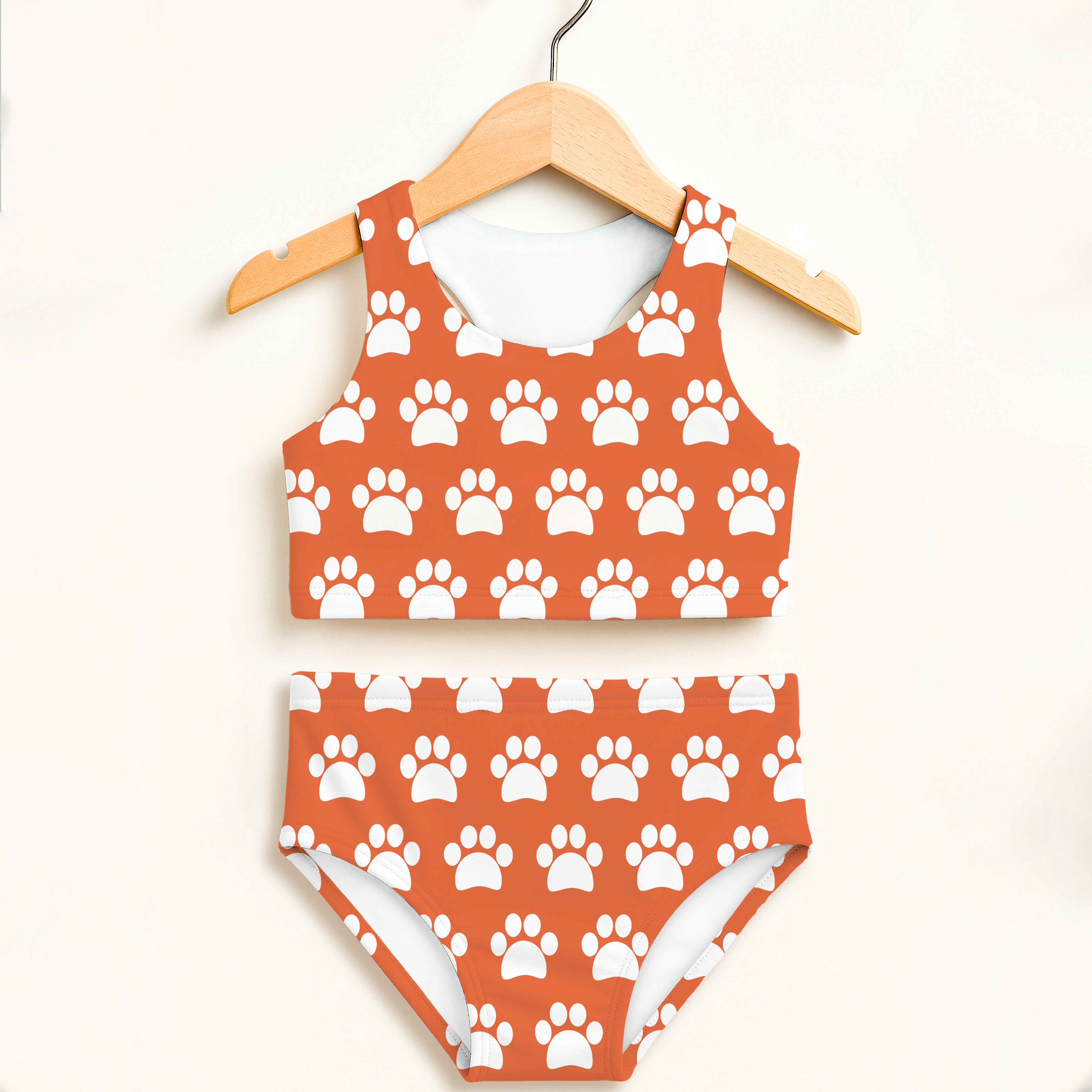 Girls orange two-piece swimsuit with white paw print pattern hanging on wooden hanger with upf 50+ protection