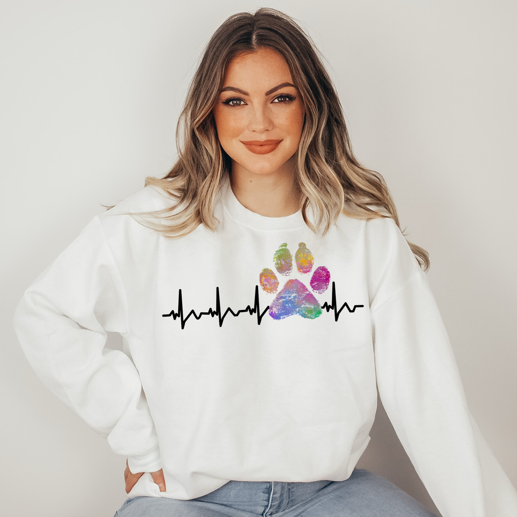 Woman wearing a white sweatshirt with a colorful paw print and heartbeat design on a plain background