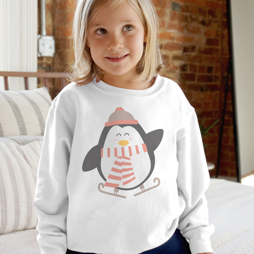 White long-sleeved kids sweatshirt with a cartoon penguin wearing a pink hat and scarf skiing on ice for holiday wear