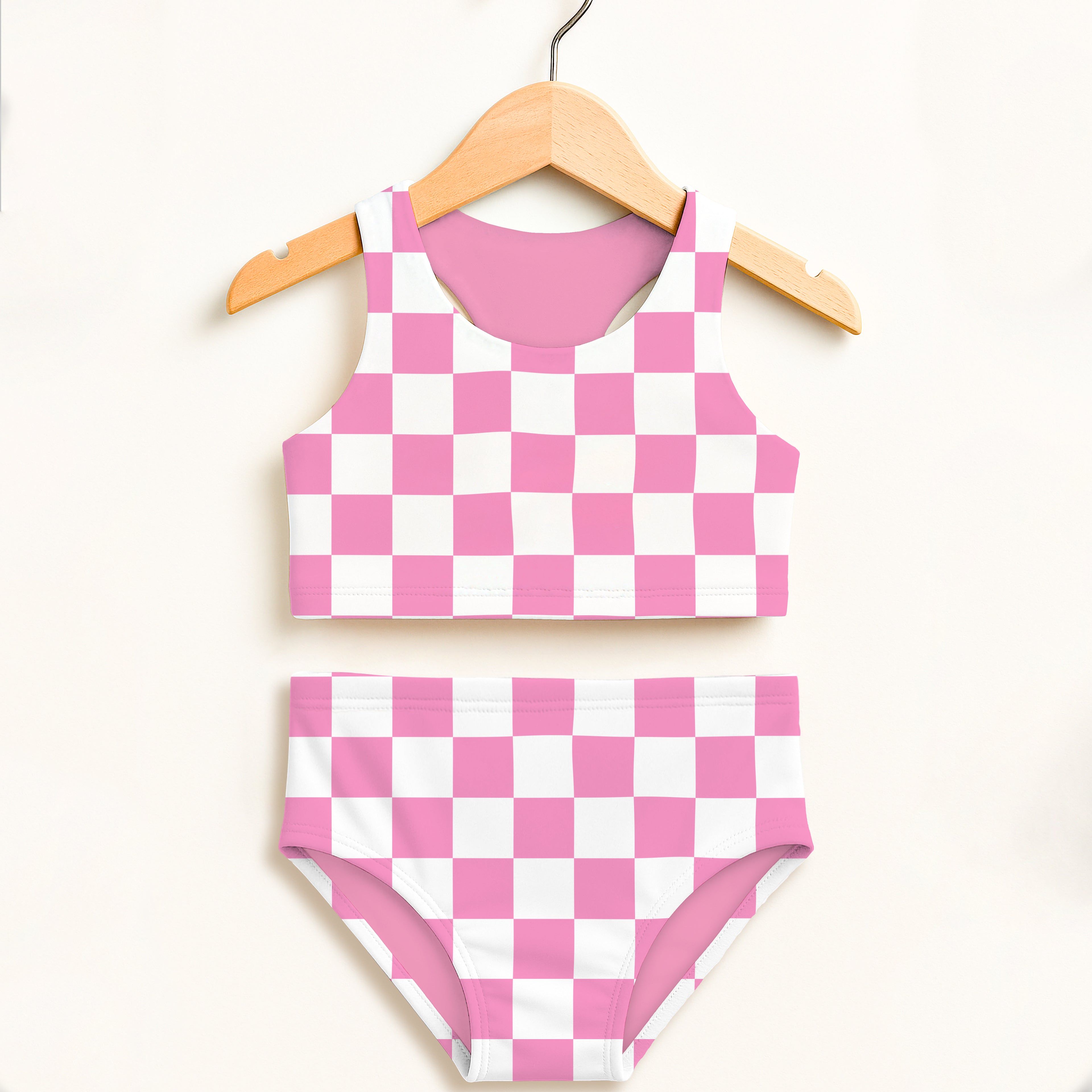 Girls pink and white checkered two-piece swimsuit with double layered fabric and upf 50 plus hanging on wooden hanger