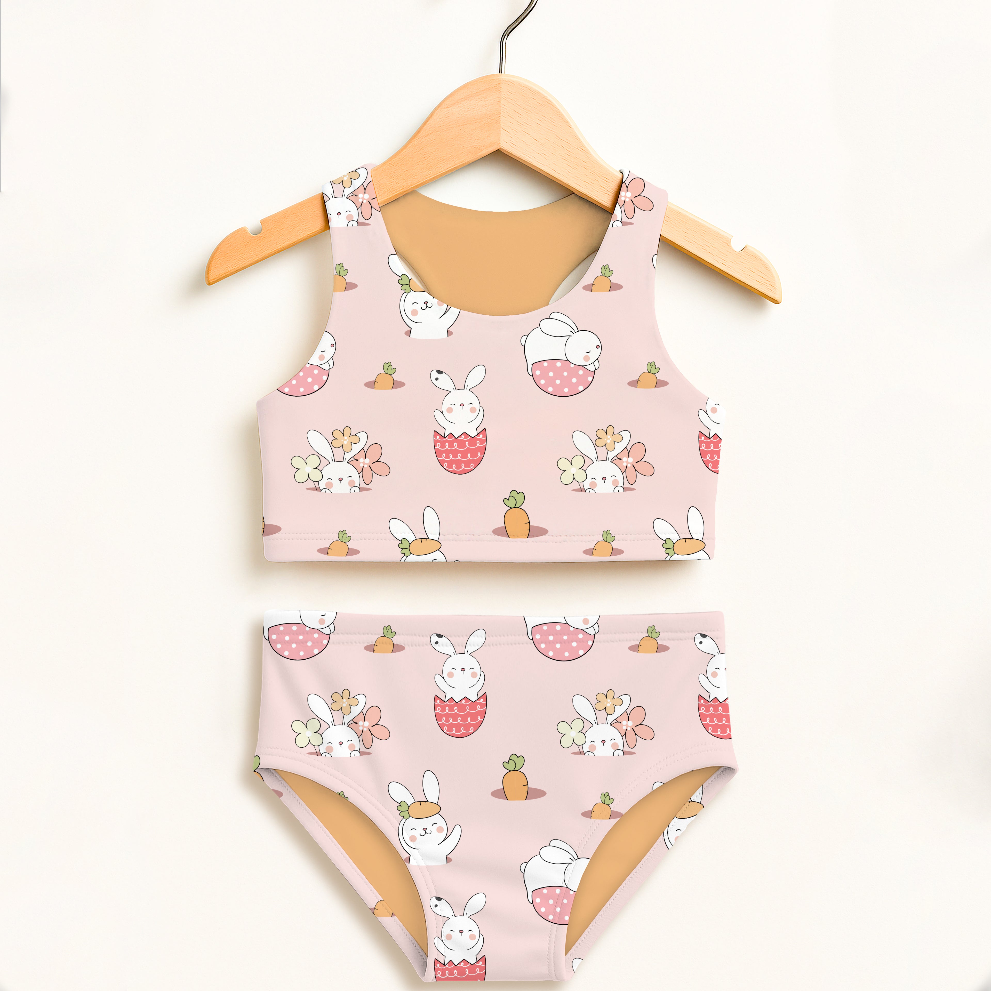 Girls pink bunny Easter two-piece swimsuit with white cartoon bunnies carrots soft pastel background UPF 50 plus