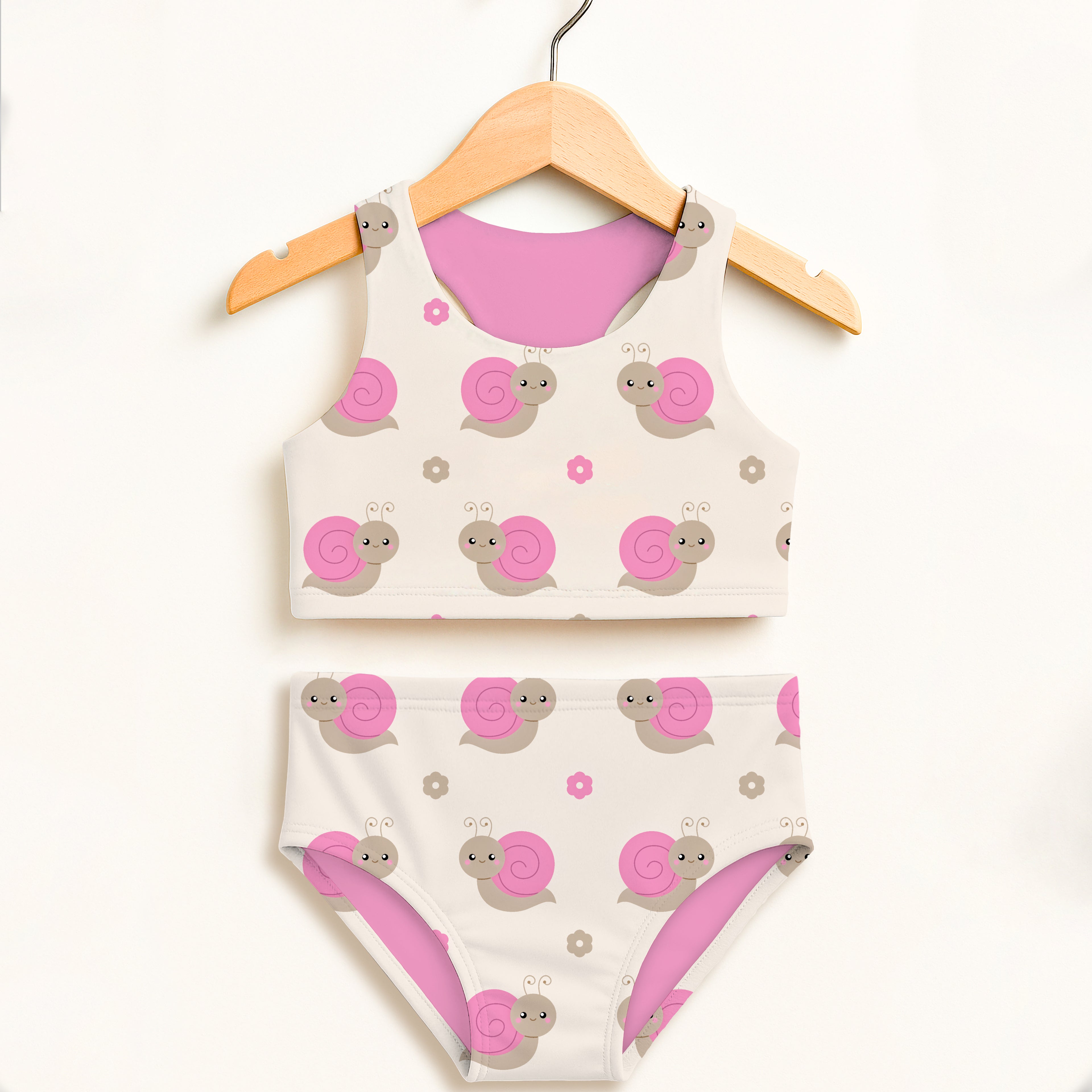 A charming white girls pink snail two piece swimsuit set with playful pink and gray snails displayed on a wooden hanger