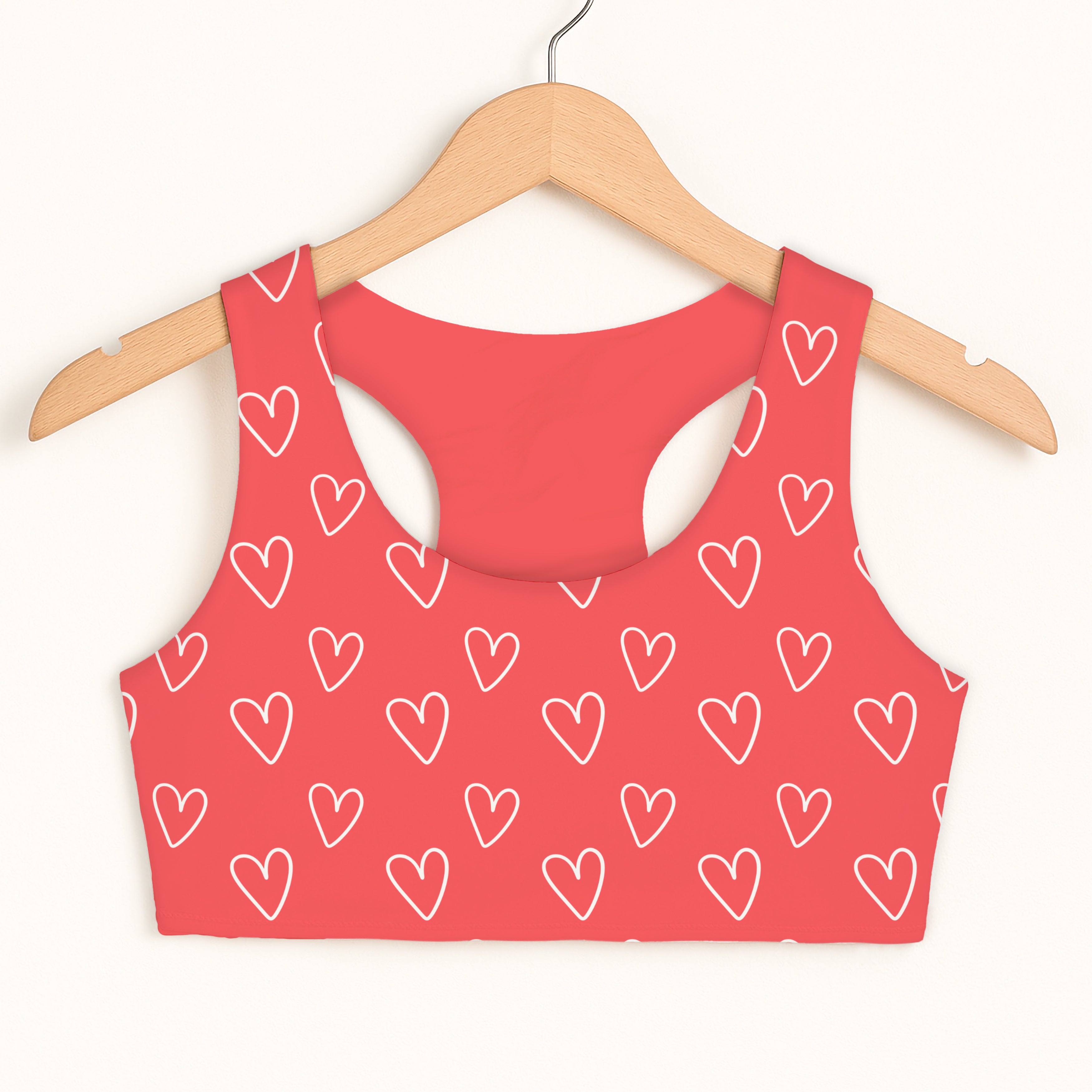 A coral pink girls sports bra with white heart pattern quick drying double layered comfort on wooden hanger