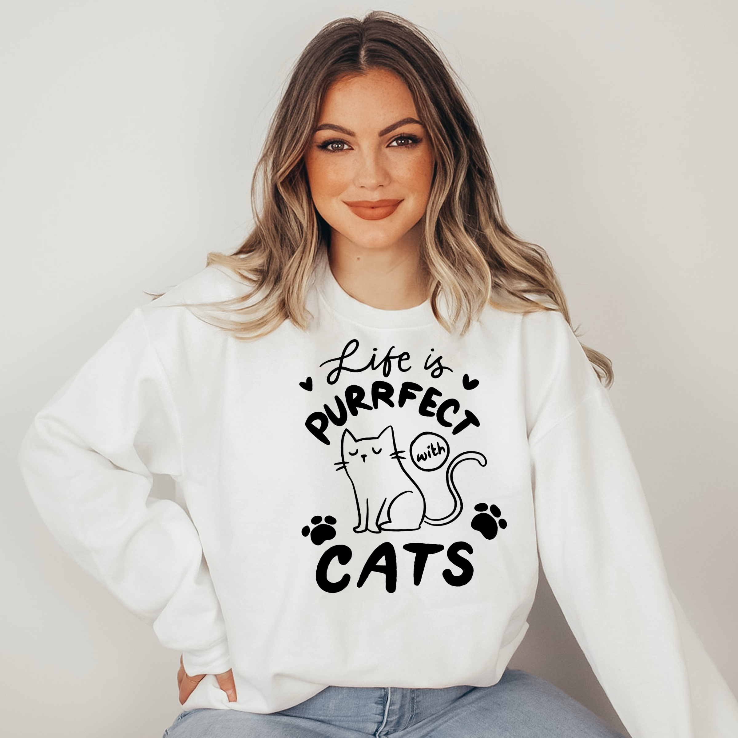 Woman wearing a white sweatshirt with a cat-themed design and text.