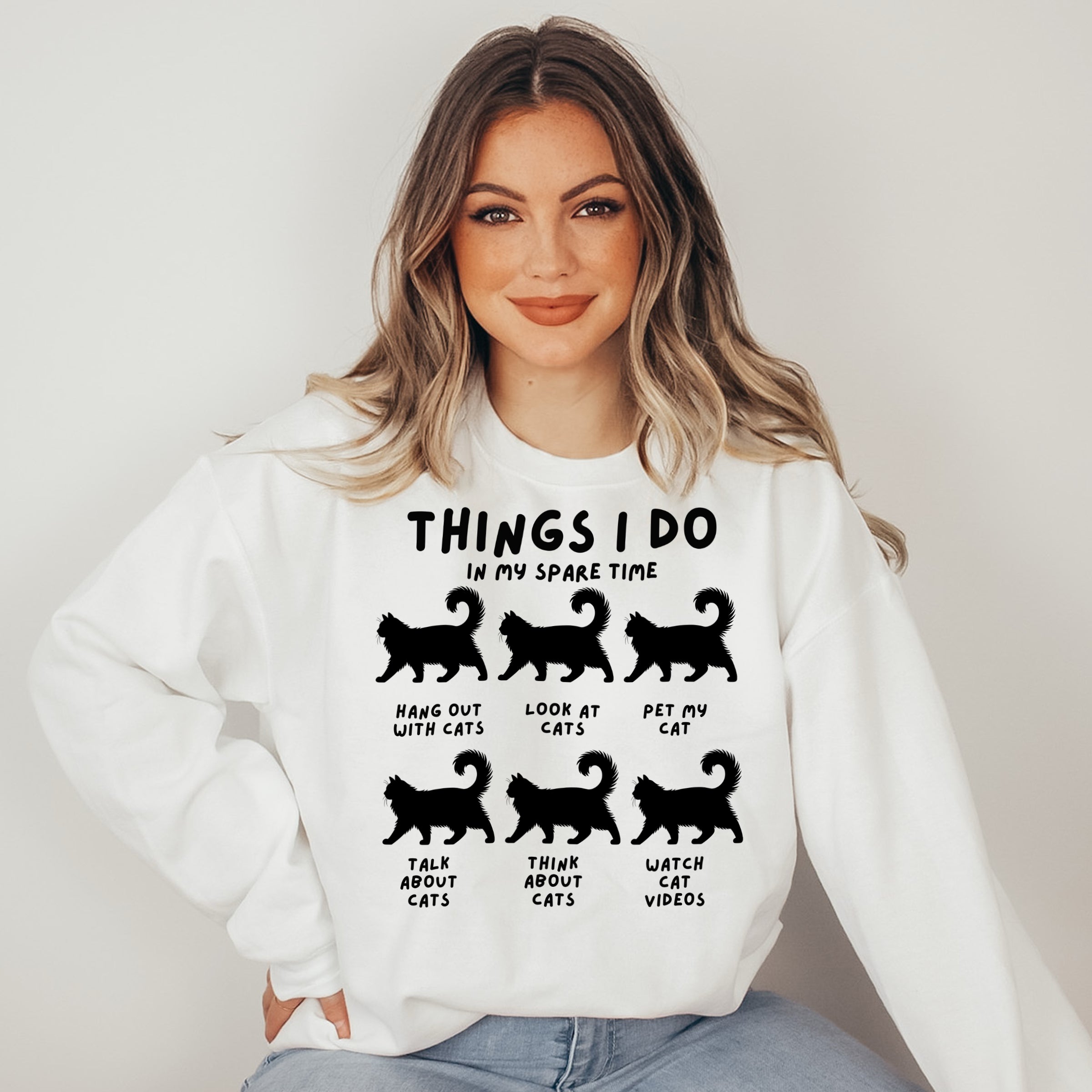 Woman wearing a white sweatshirt with black text and cat illustrations on a plain background