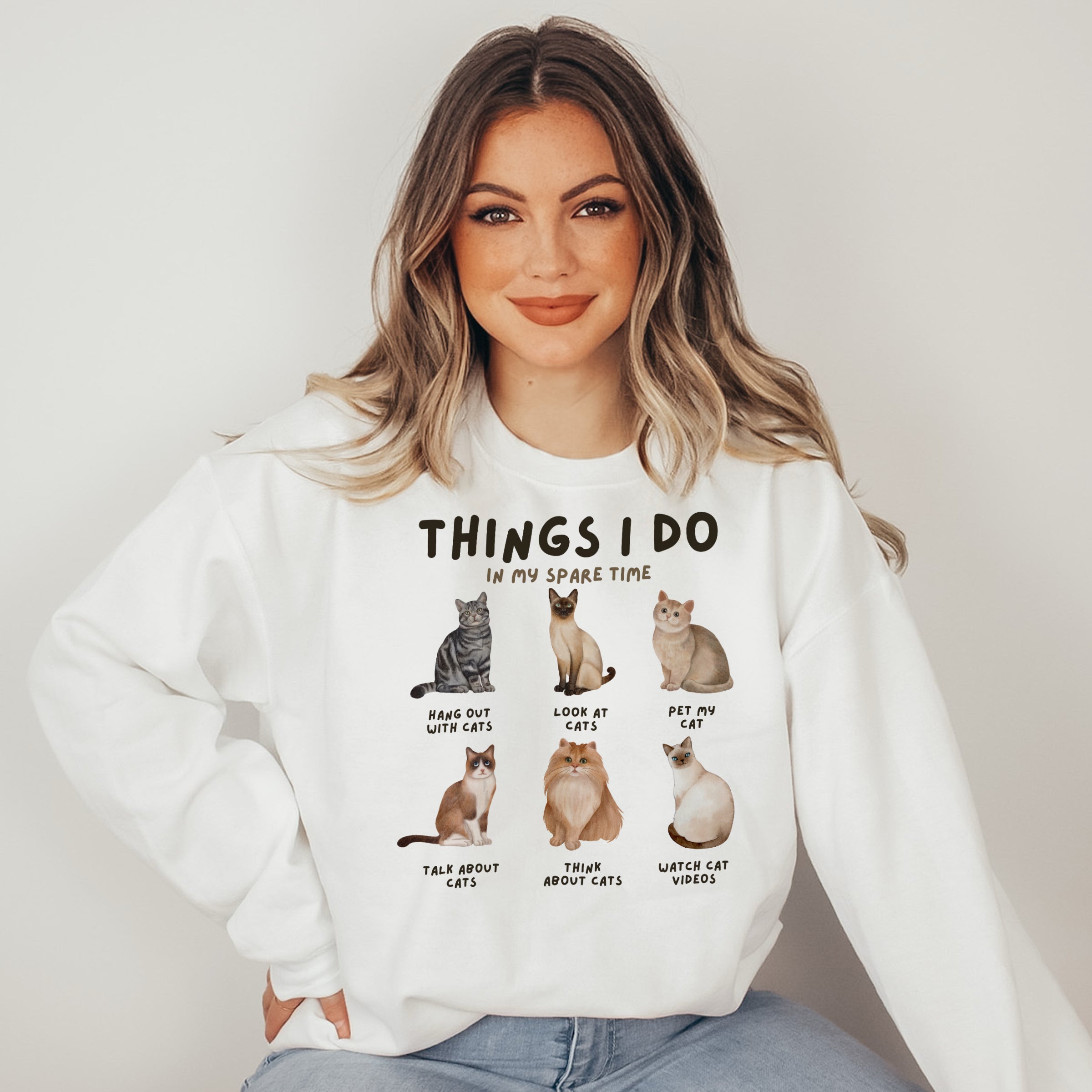 Woman wearing a white sweatshirt with cat illustrations and text.