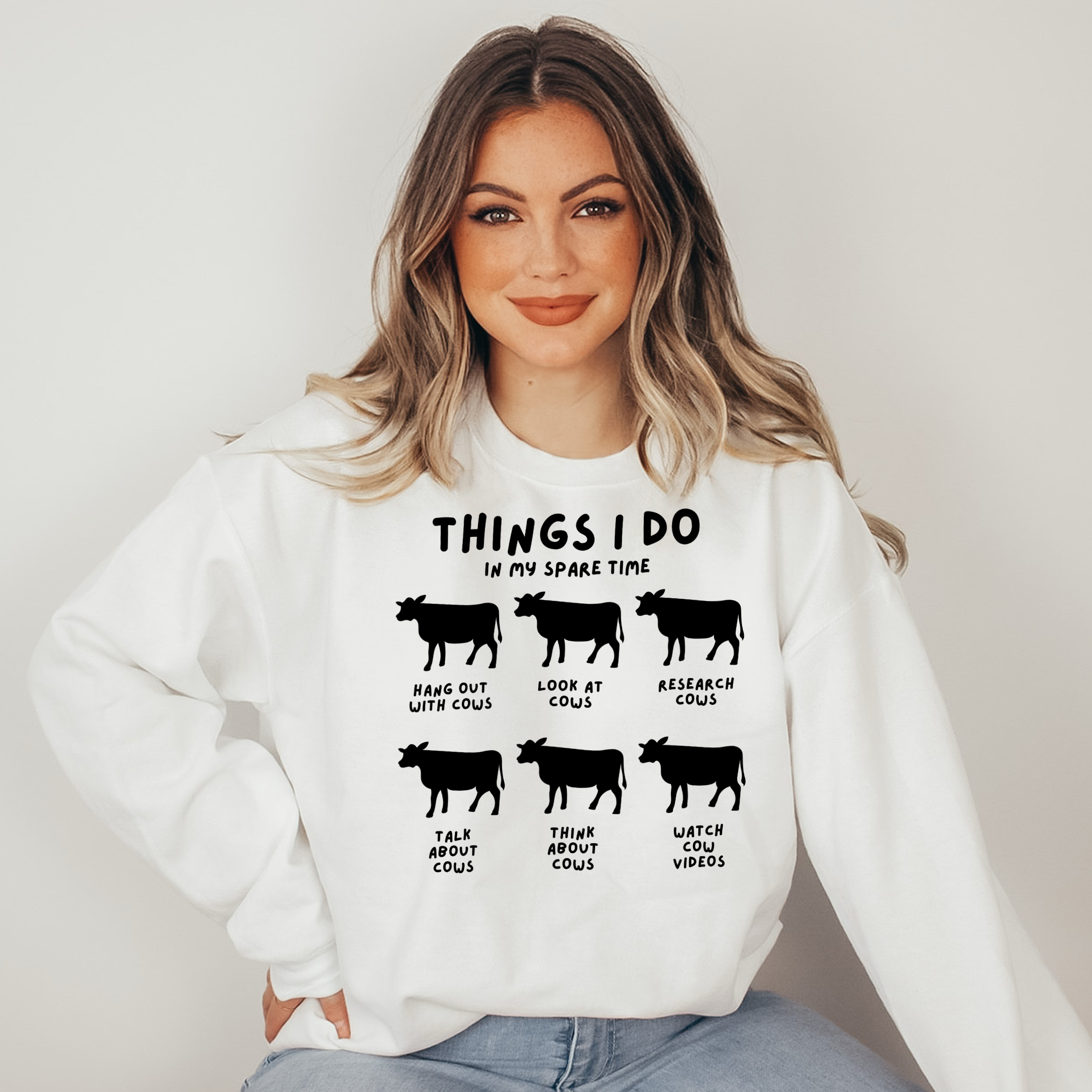 Woman wearing a white sweatshirt with cow-themed text design on a plain background