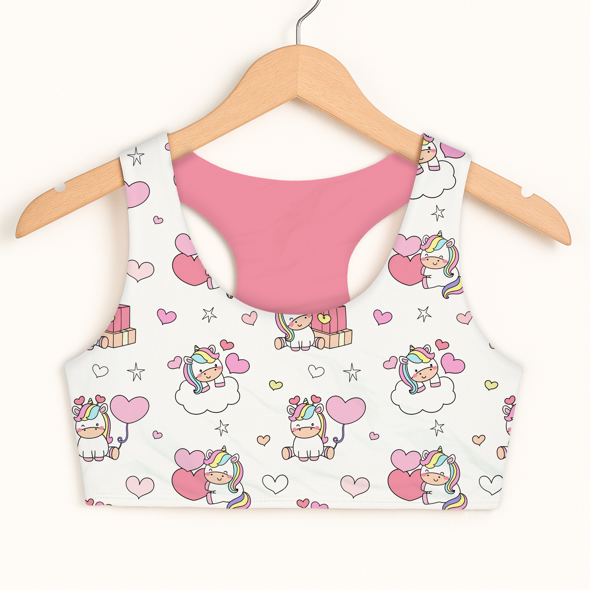 Pink girls sports bra with a white crop top featuring unicorn designs on a hanger against a white background.